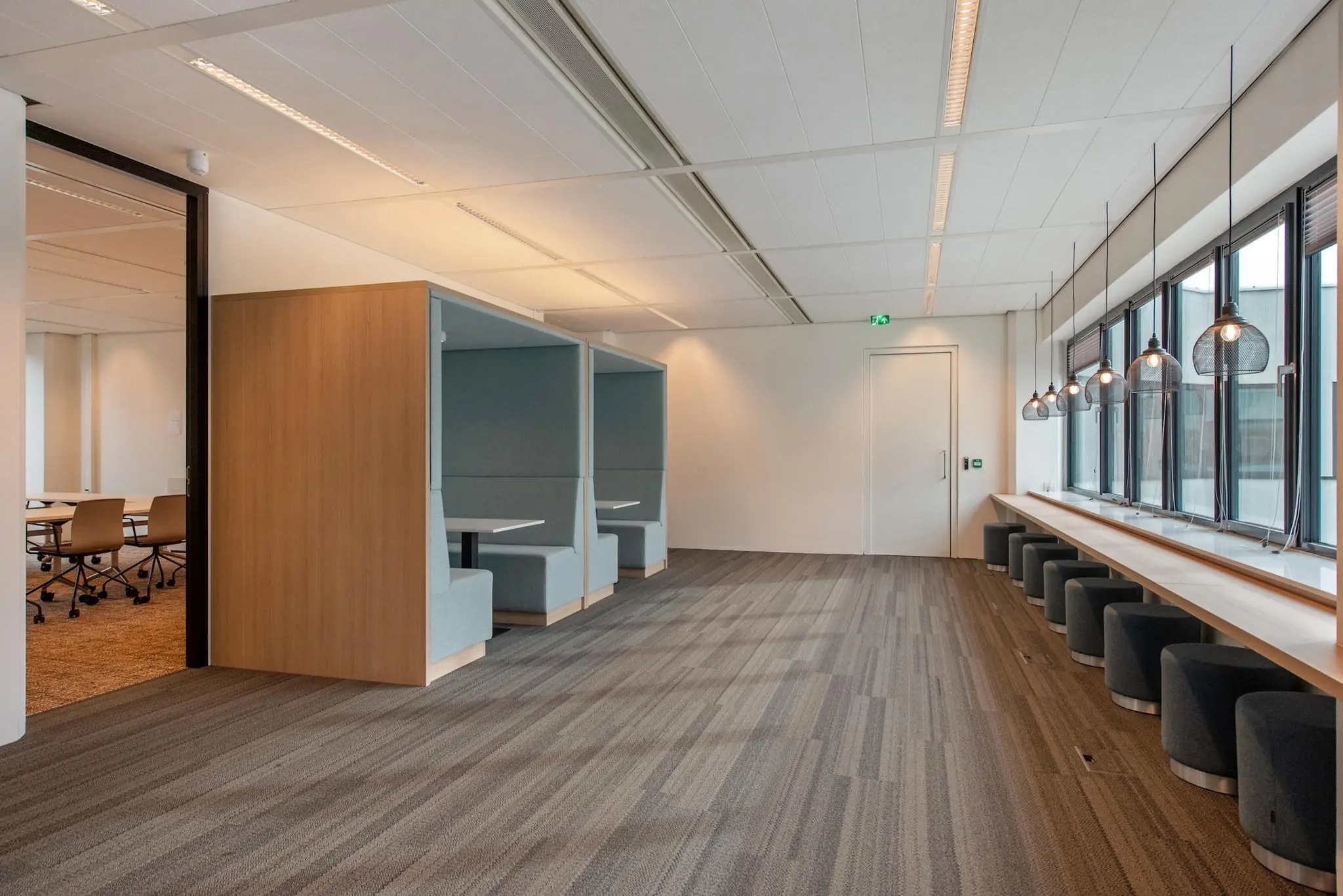 Moderne open kantooruimte aan de Grote Marktstraat met flexibele zitplekken en werkhokjes langs een raam met hanglampen.